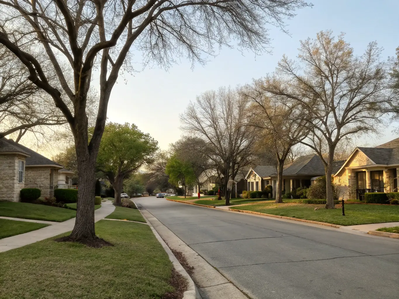 A picturesque suburban street in Lindale, Texas, lined with well-maintained houses and green lawns, under a clear blue sky, showcasing the charm and tranquility of a family-friendly neighborhood.
